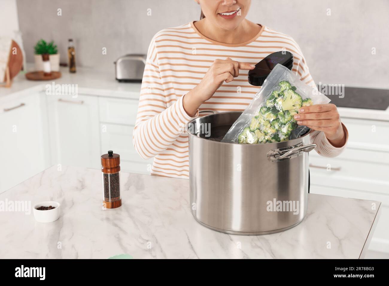 Woman putting vacuum packed broccoli into pot and using thermal immersion circulator, closeup
