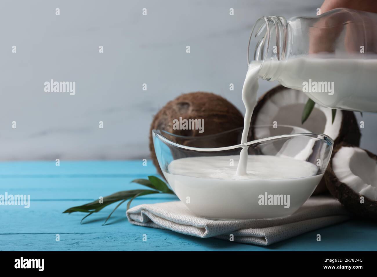 Woman pouring delicious coconut milk into bowl on light blue wooden table, closeup. Space for text Stock Photo
