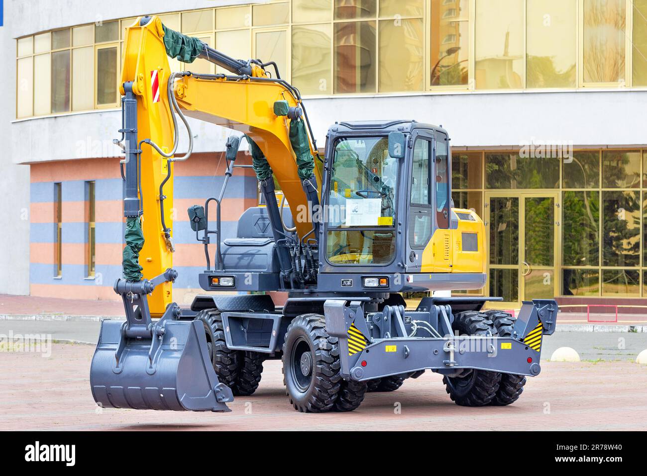 New wheeled construction excavator against the backdrop of a building on a sunny day. Stock Photo