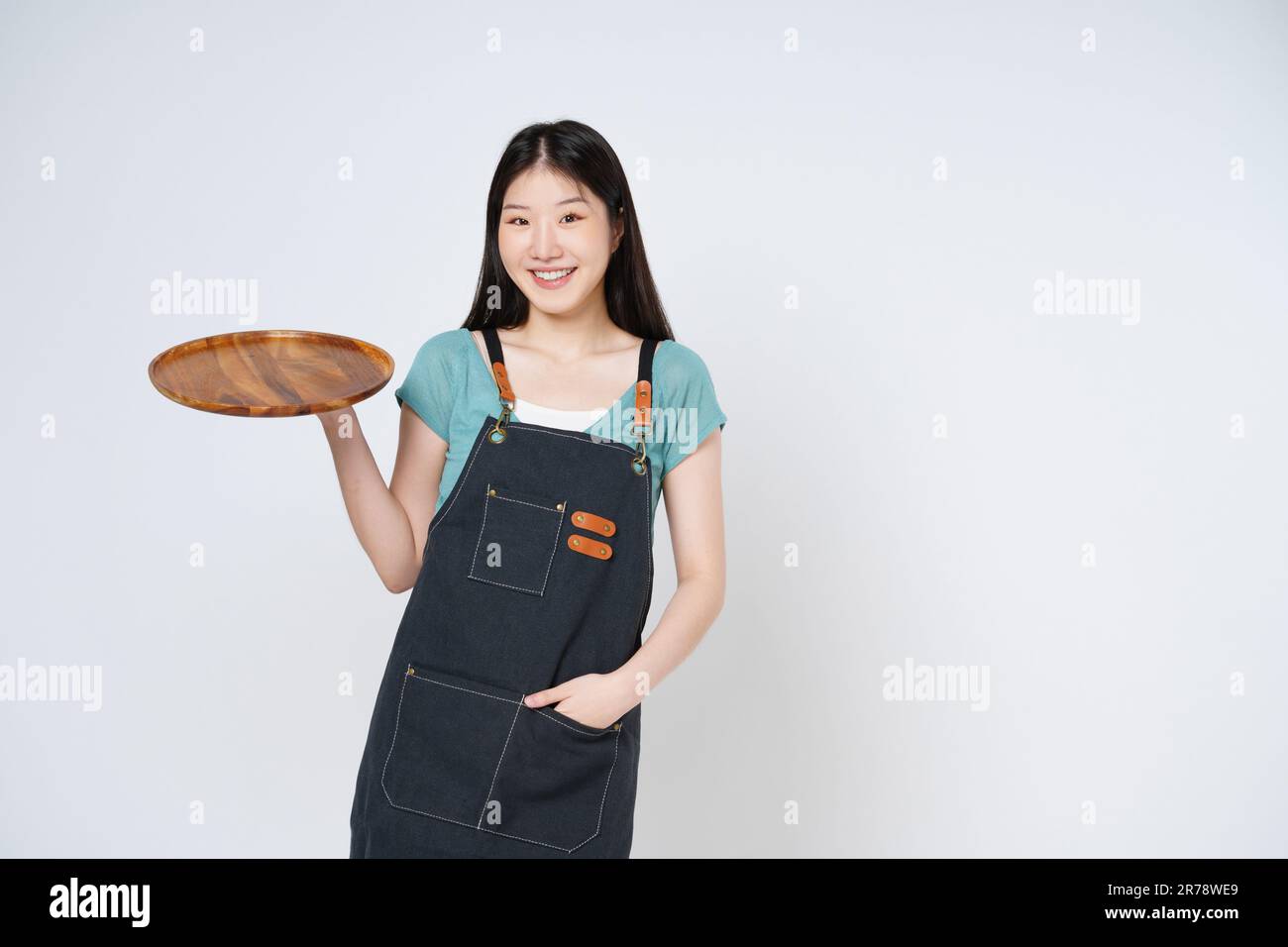 Young woman wearing apron and holding empty plate isolated on white background. Stock Photo