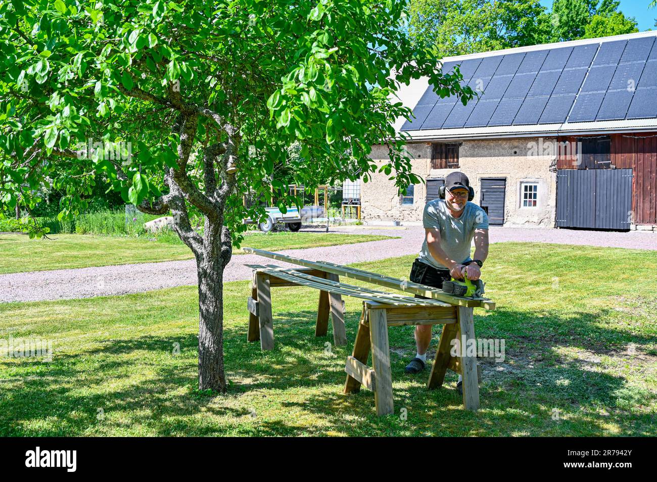 man standing in garden cutting planks with circle saw Stock Photo - Alamy