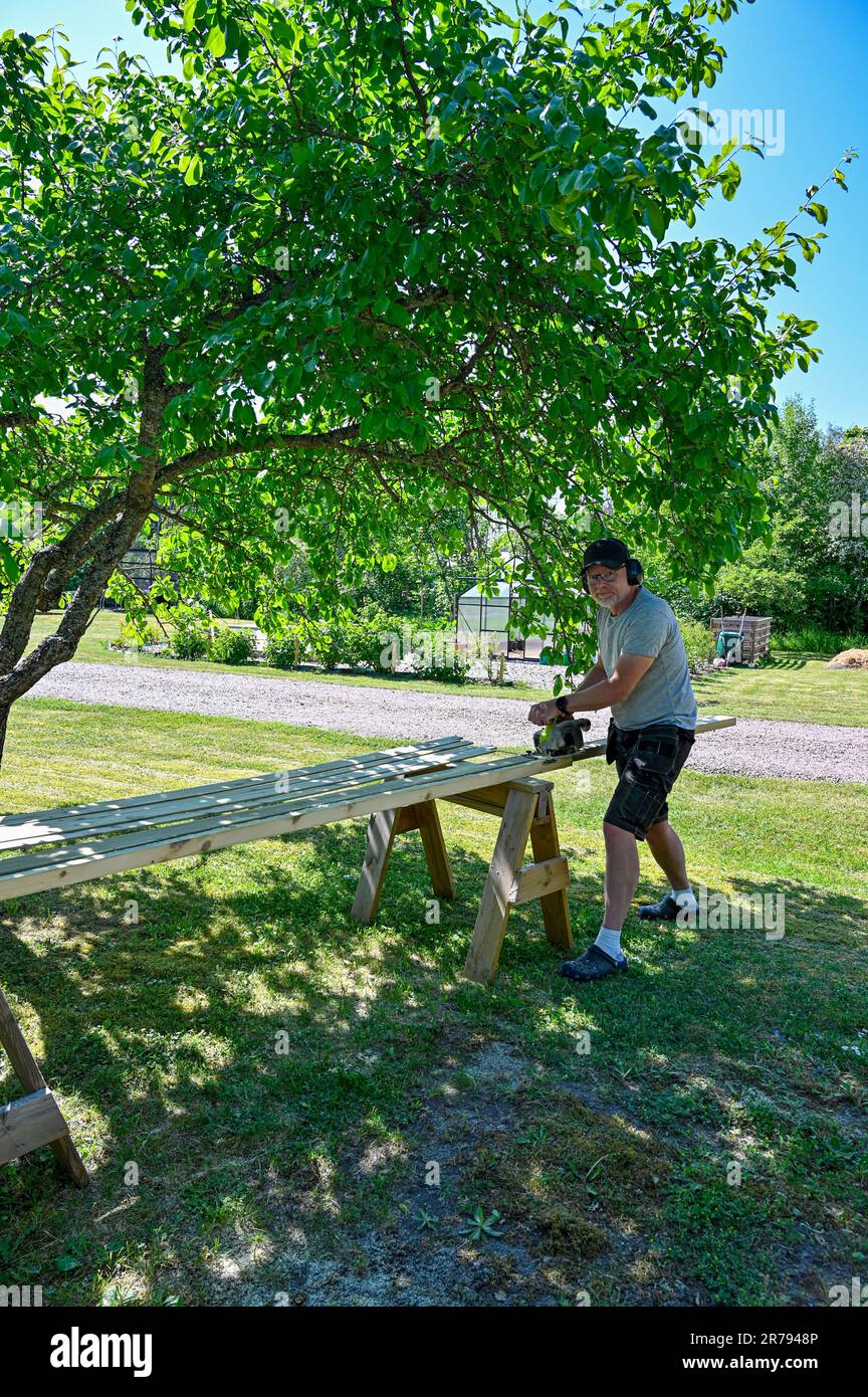 man standing in garden cutting planks with circle saw Stock Photo - Alamy
