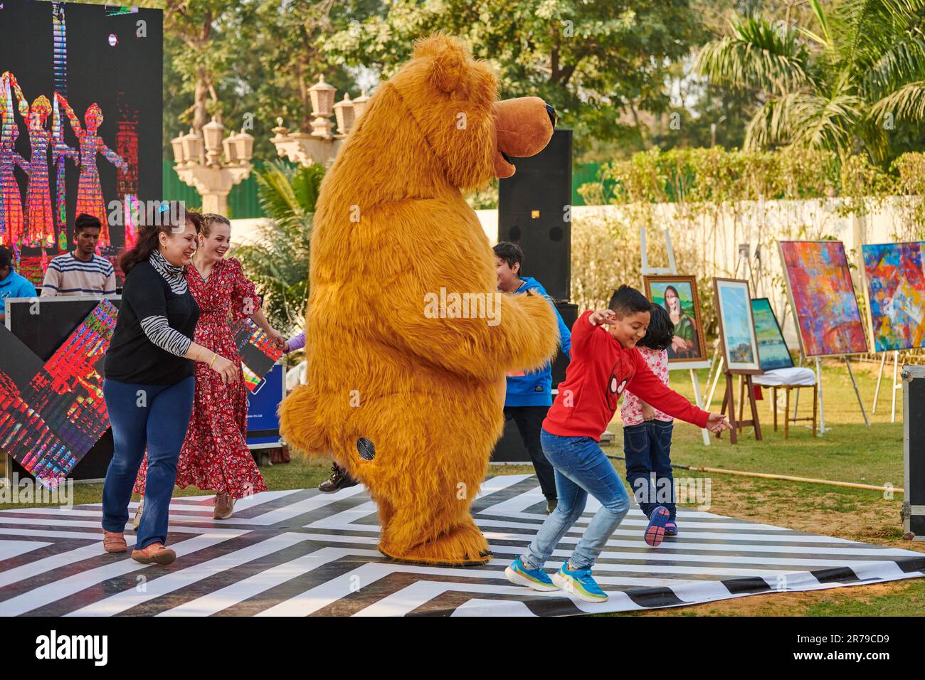 New Delhi, India - 10.12.2022 - Children outdoor party dancing with brown teddy bear, funny children games with big toy teddy bear, happy childhood co Stock Photo