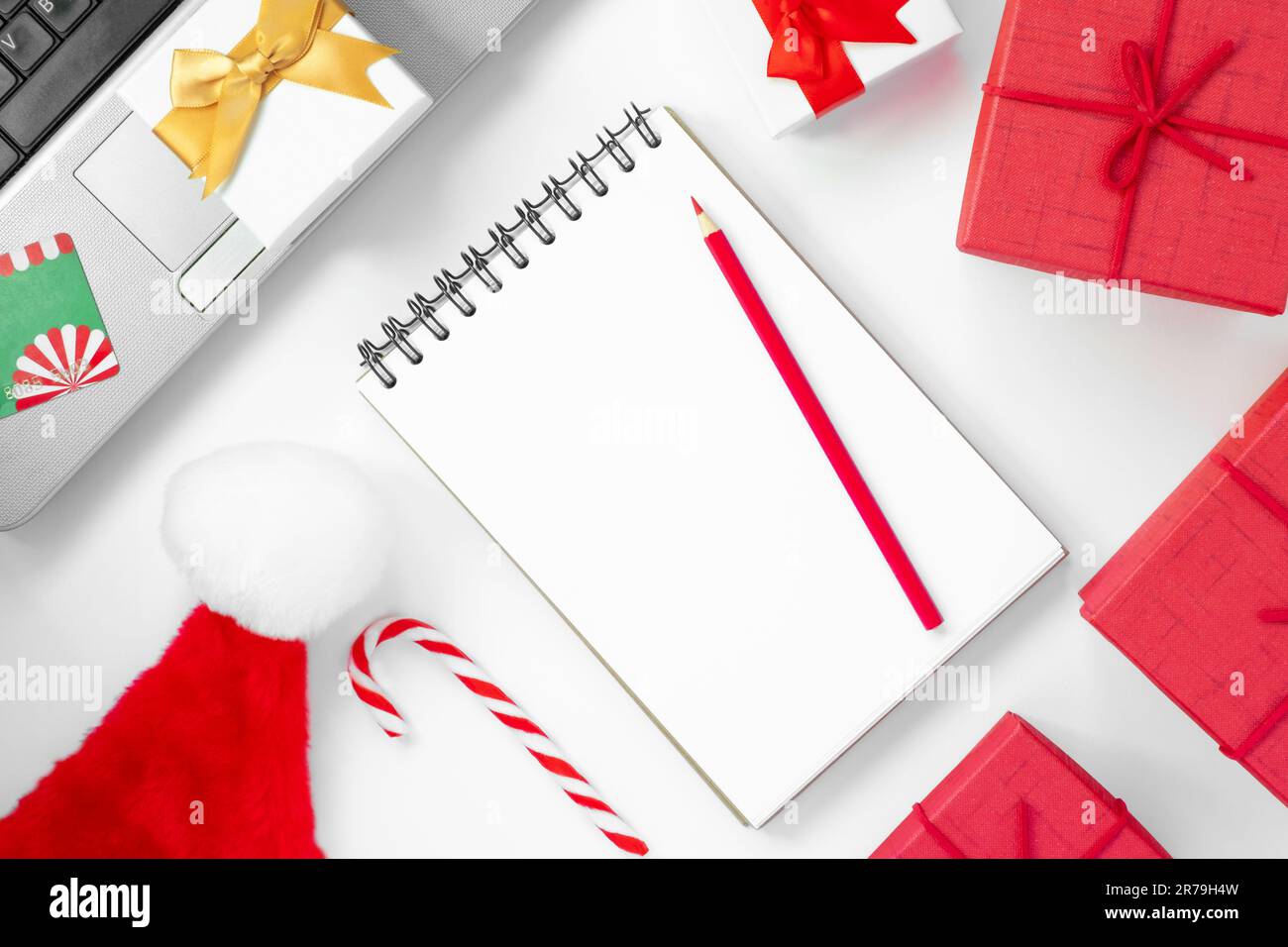 Christmas online shopping flat lay. Notebook with pencil. Shopping list. Credit card, Laptop, Candy and Christmas presents on white table. Page for yo Stock Photo