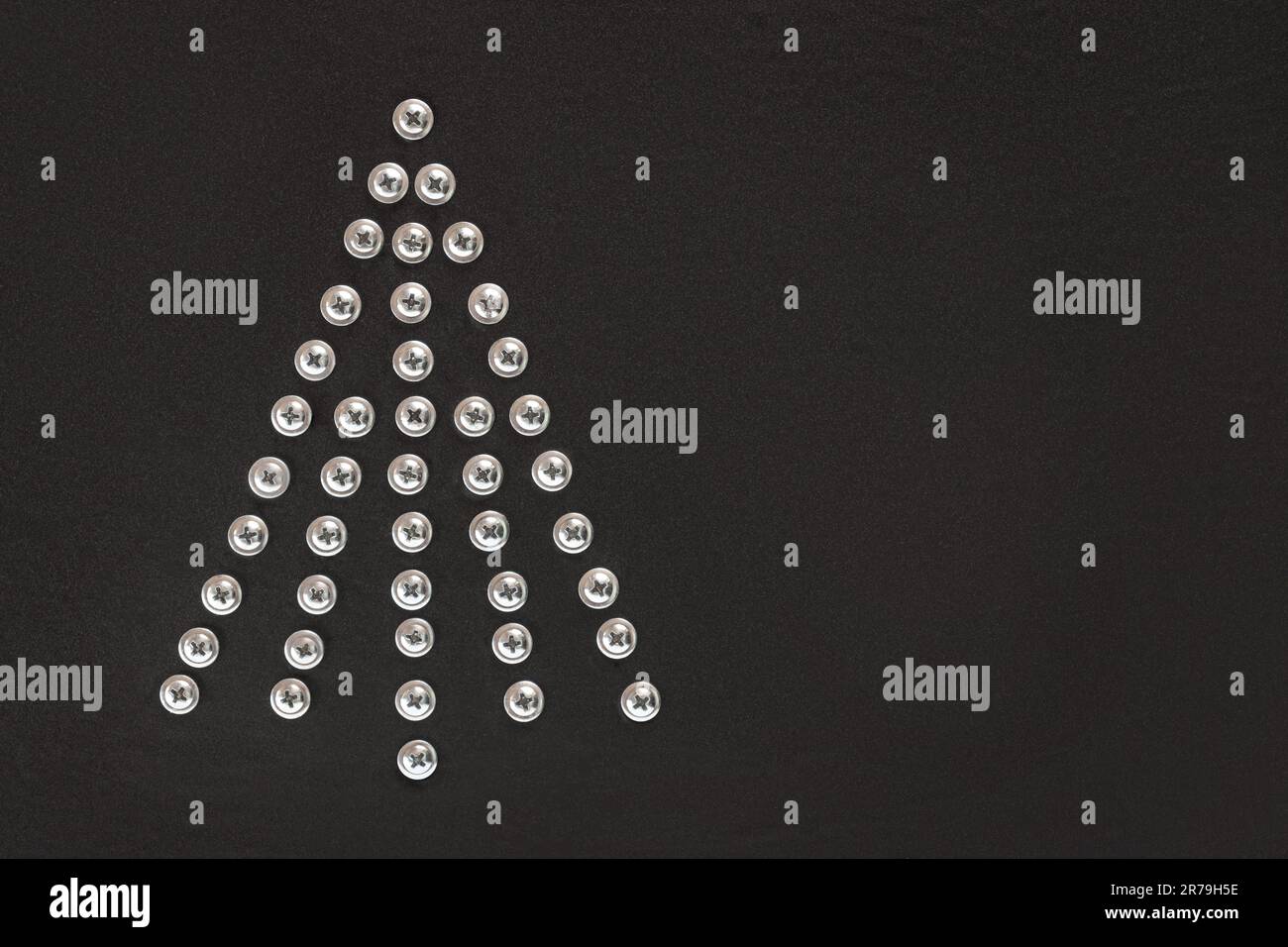 Christmas tree of screws on a black background. Flat lay. Copy space. Unusual Christmas tree made of construction tools. Creative Industrial greeting Stock Photo