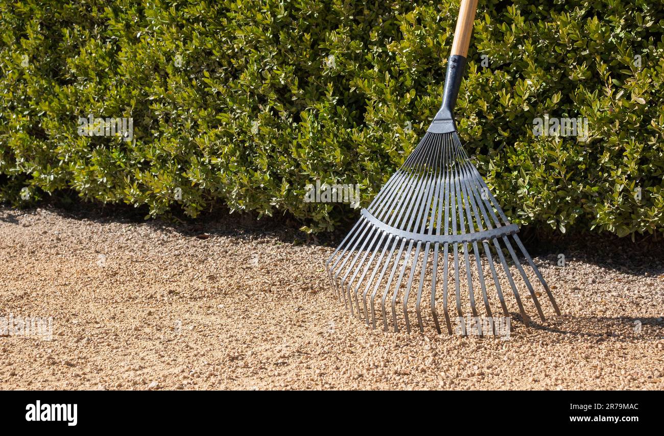 A gardening tool, a rake, laid in the middle of a gravel pathway