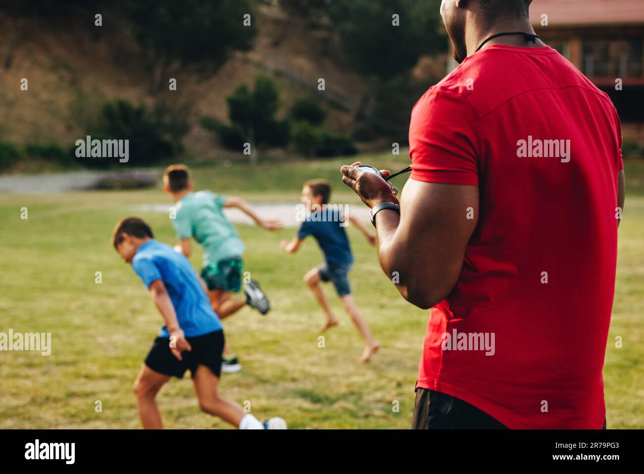 Sports trainer coaching a primary school team. PE teacher having a running session with a group of elementary school children. Sports and recreation i Stock Photo