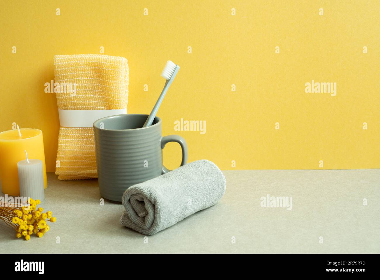 Bathroom shower towel and toothbrush, cup, candle, dry flower on gray table. yellow background Stock Photo