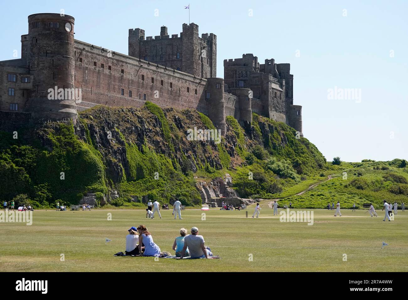 A charity cricket match takes place under the back drop of Northumberland's Bamburgh Castle. The Met Office has issued guidance that most of the UK will meet heatwave criteria this week, and an amber alert for hot weather has been issued by the UK Health Security Agency (UKHSA). Picture date: Wednesday June 14, 2023. Stock Photo