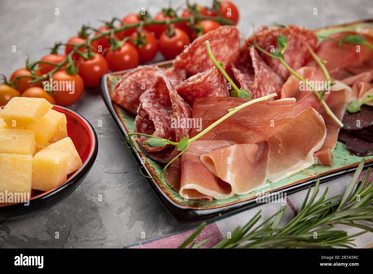 A wooden tray featuring a selection of cured meats, cheeses and fresh fruits, served on a white plate Stock Photo