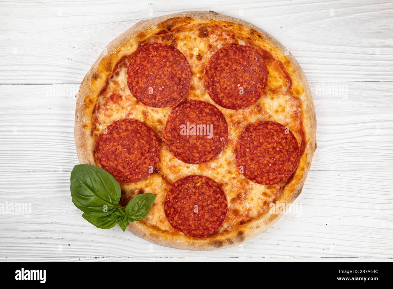 An image of a freshly made pepperoni pizza served with a basil plant in the background on a wooden table Stock Photo