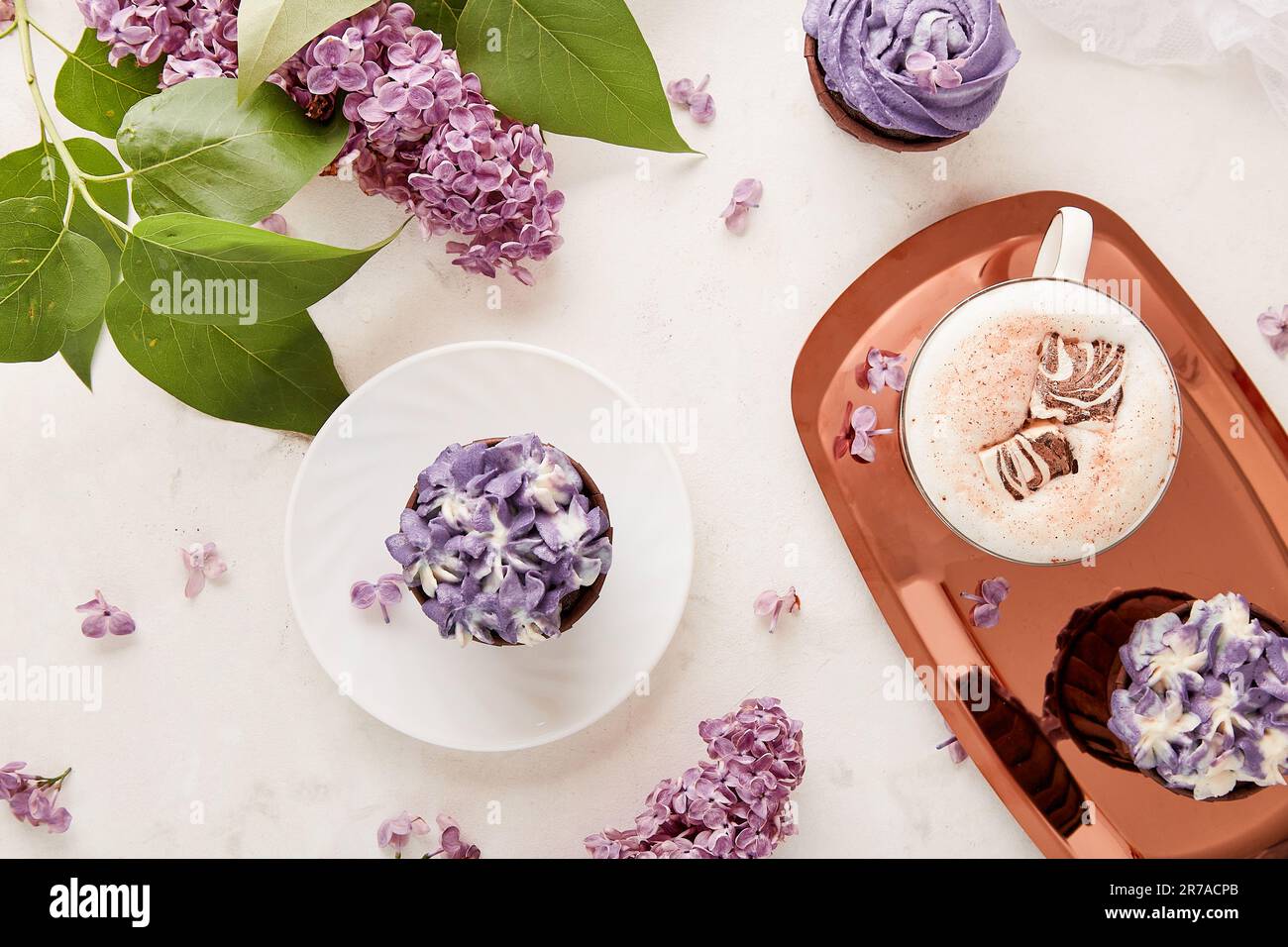 Floral purple cupcakes desserts, coffee cup with melted marshmallow among lilac flowers background flat lay Stock Photo