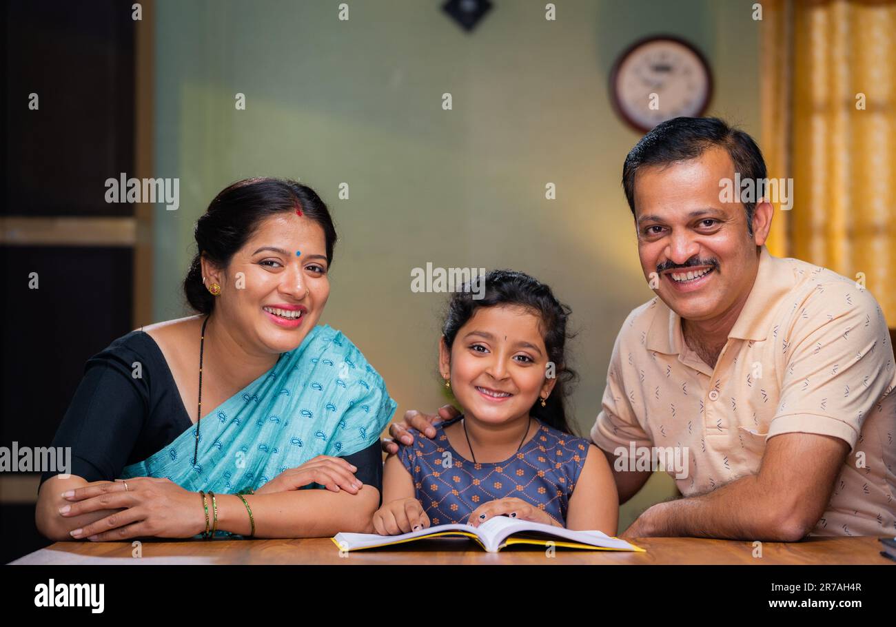 Happy indian parents with daughter looking camera at home while teaching to kid - concept of family relationship, parenthood and education Stock Photo