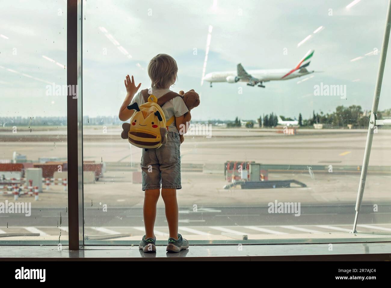 Child, watching from the window of the airport the planes, taking off and landing while waiting