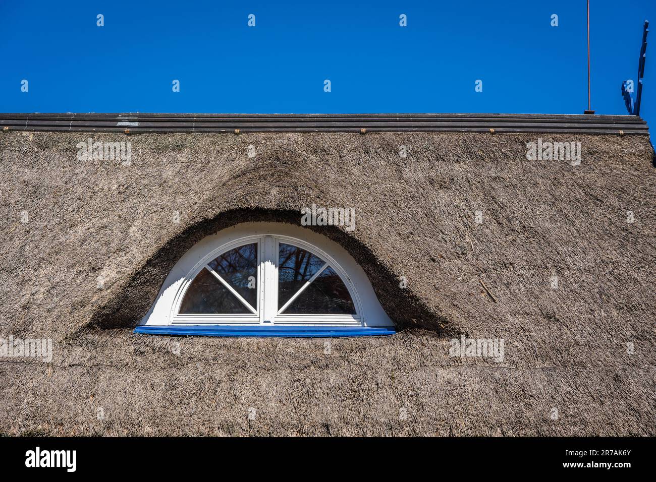 Fragment of an old straw or reed roof with a semi-circular dormer roof window. Stock Photo