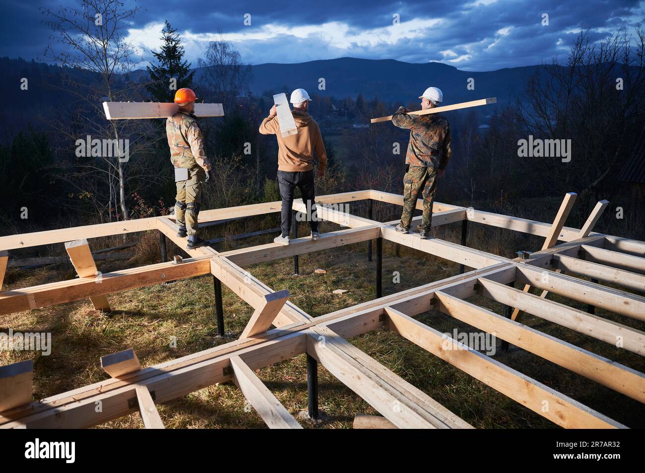 Men workers building wooden frame house on pile foundation. Back view