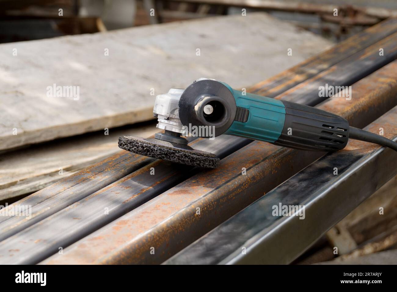 Not new electric angle grinder tool lies on a rust metal square tube