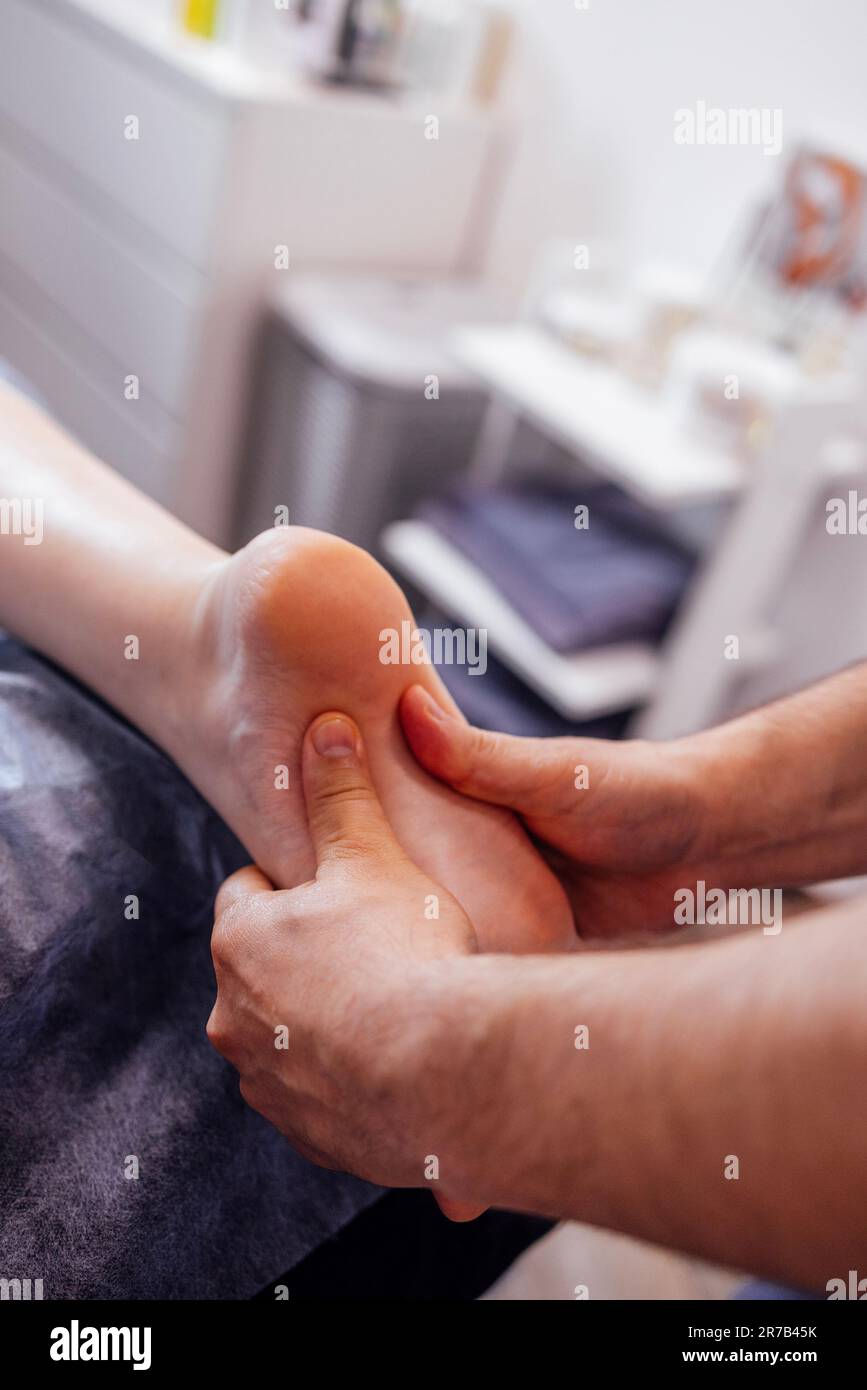 Close up of female foot getting gentle massage. Masseuse holds woman leg in her hands. Young client lies and enjoys relaxing procedure in beauty salon Stock Photo