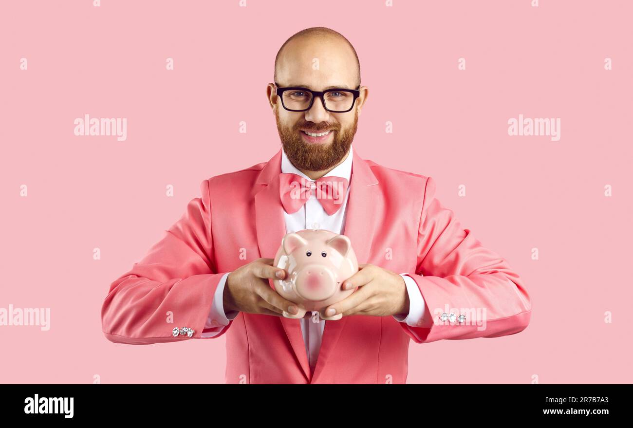 Extravagant cheerful man in suit holding piggy bank in form of pig ...
