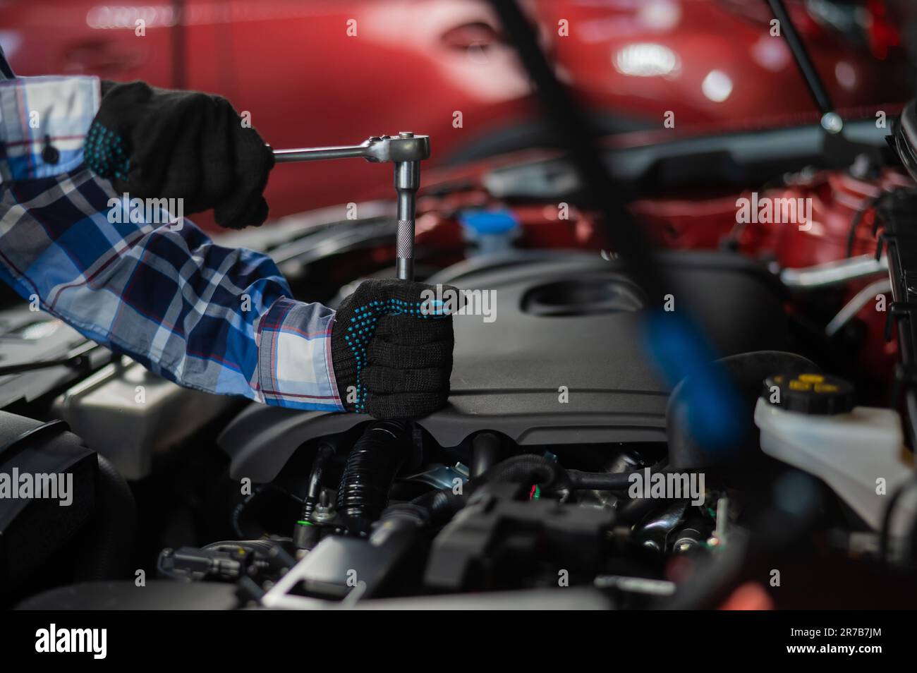 Female auto mechanic unscrewing a nut to replace a car spark plug Stock