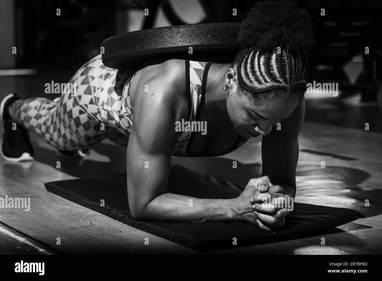 An athletic female fitness enthusiast engaging in a weighted planking exercise, demonstrating strength, balance, and determination Stock Photo
