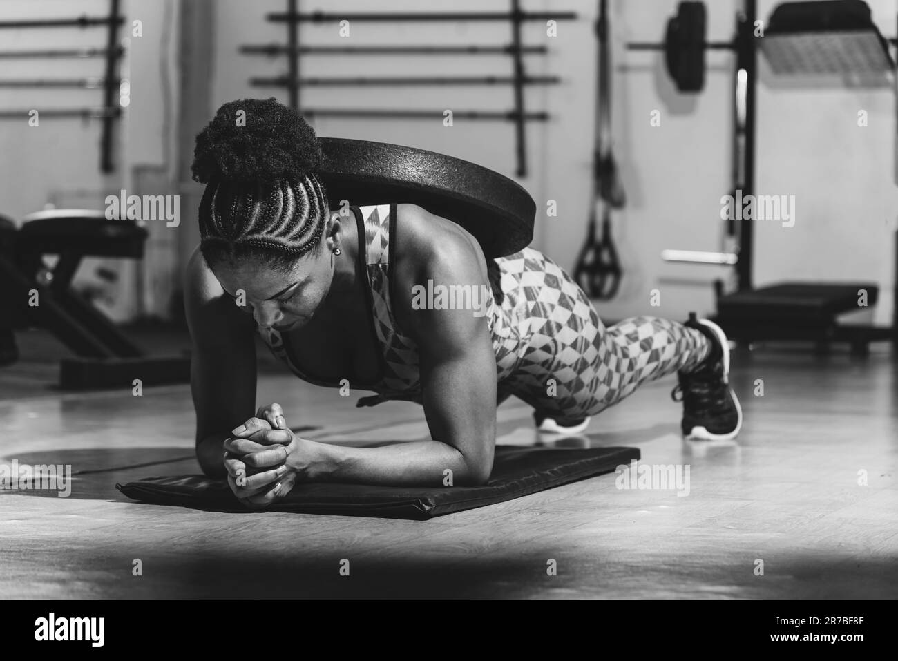 An athletic female fitness enthusiast engaging in a weighted planking exercise, demonstrating strength, balance, and determination Stock Photo