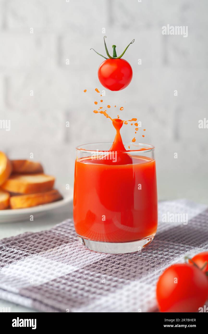 Against the background of a white brick wall, a glass of tomato juice with vegetables Stock Photo