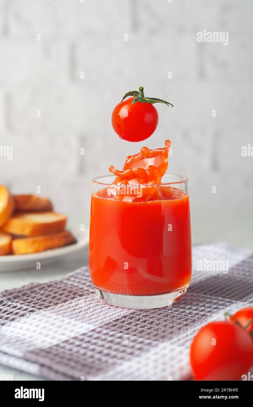 Against the background of a white brick wall, a glass of tomato juice with vegetables Stock Photo
