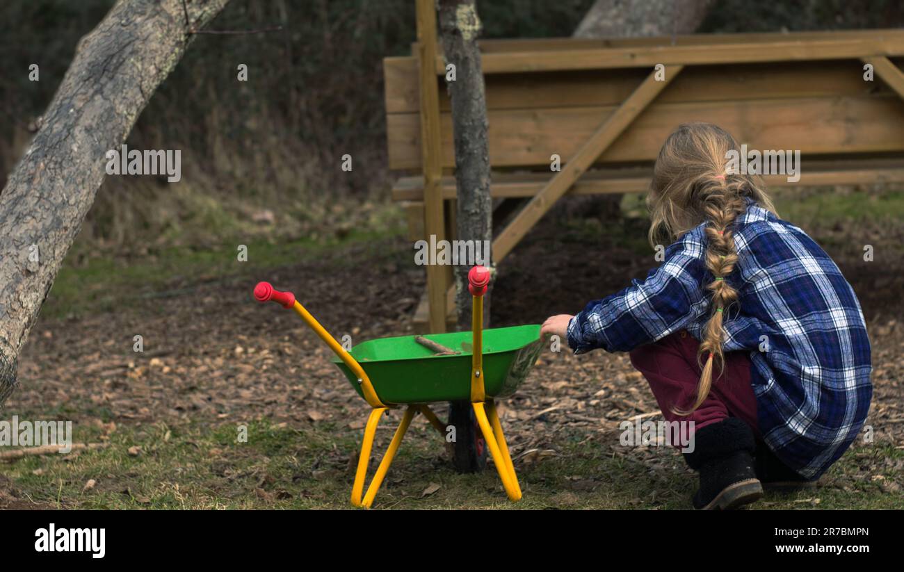 A rear view of a small girl playing with dirt in a park holding a toy ...