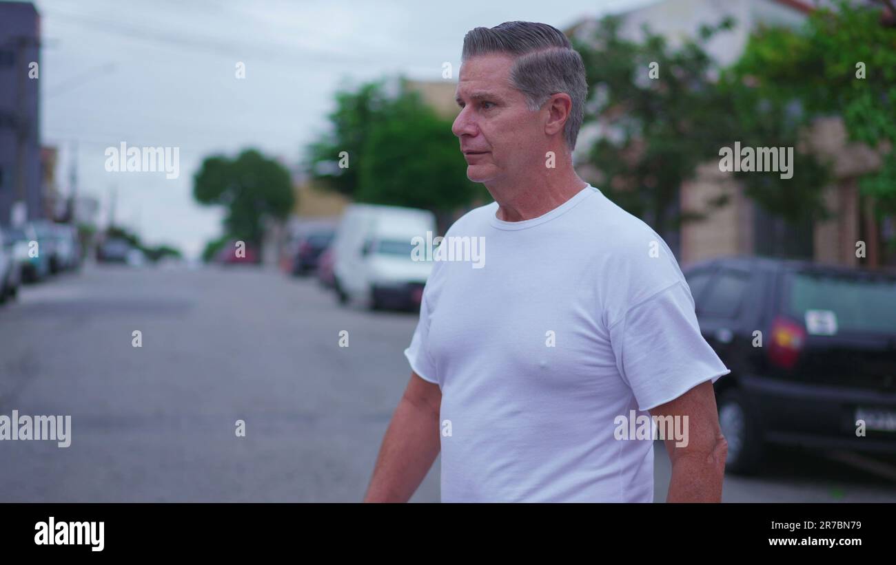 Middle-aged man crossing street and waving hello to neighbor while walking. Person walking in urban environment, casual authentic daily lifestyle Stock Photo