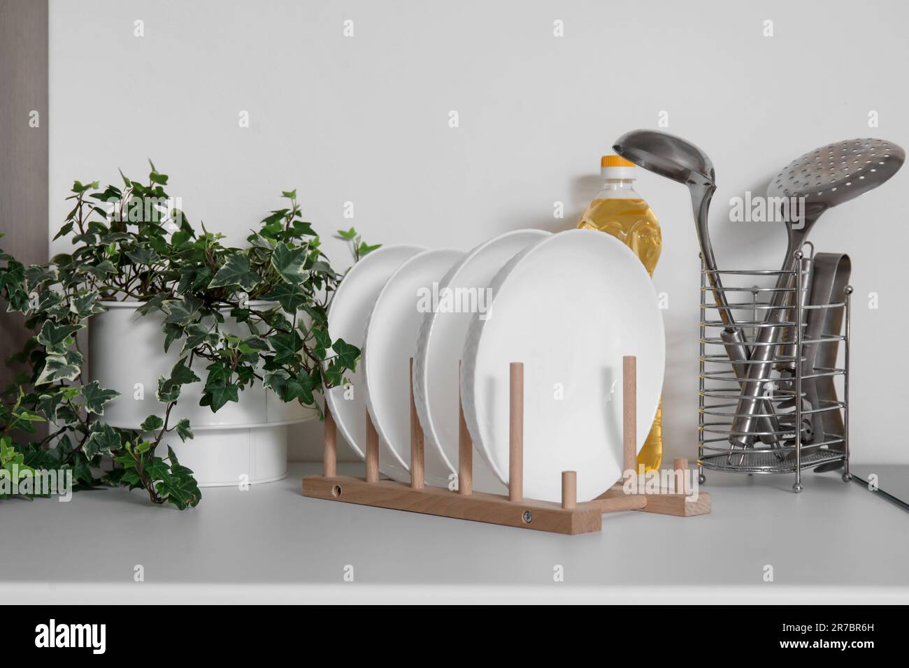 Plate rack, houseplant and utensils on white kitchen counter, closeup Stock Photo