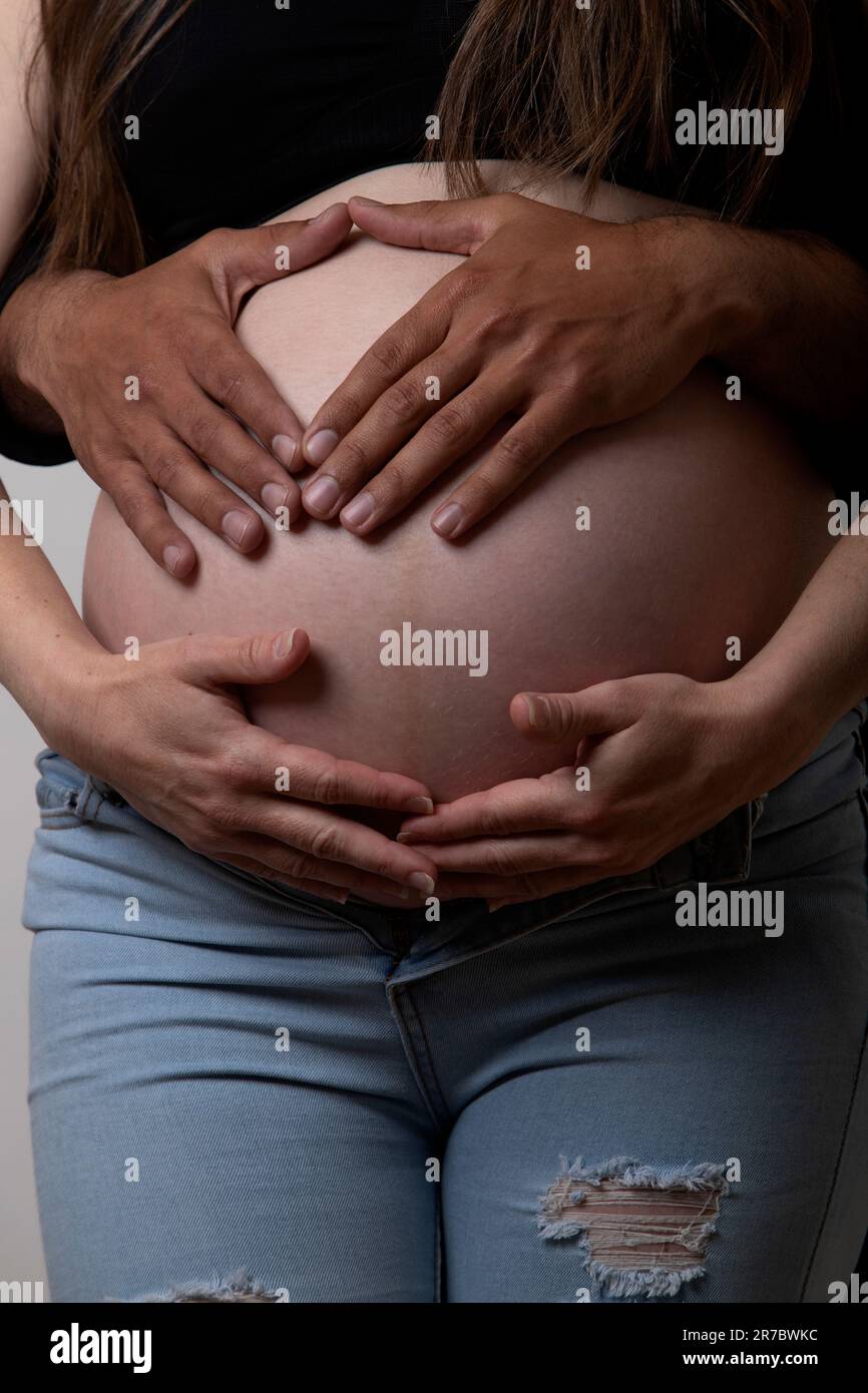 hispanic and caucasian hands on pregnant belly Stock Photo