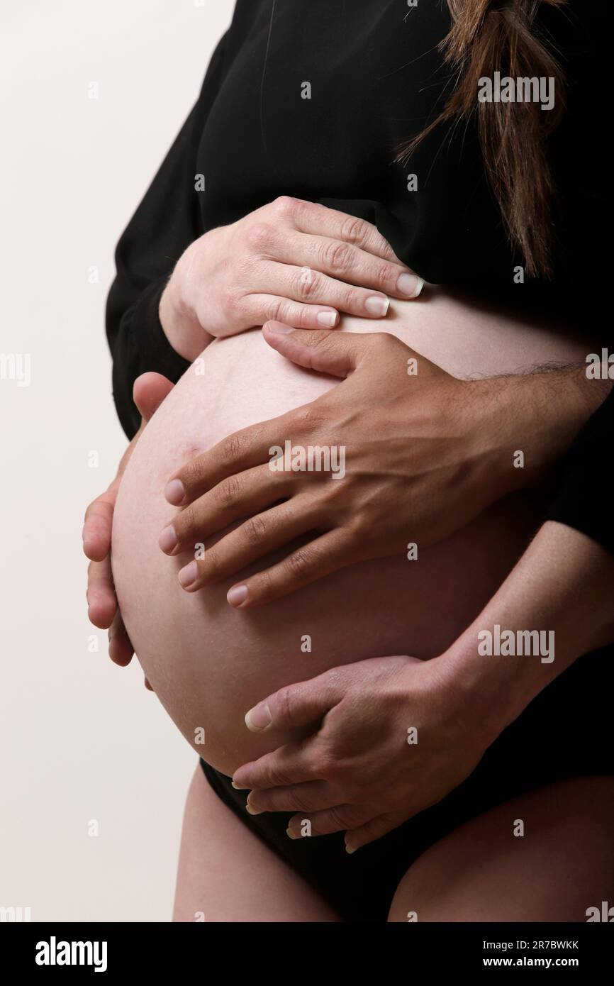hispanic and caucasian hands on pregnant belly Stock Photo
