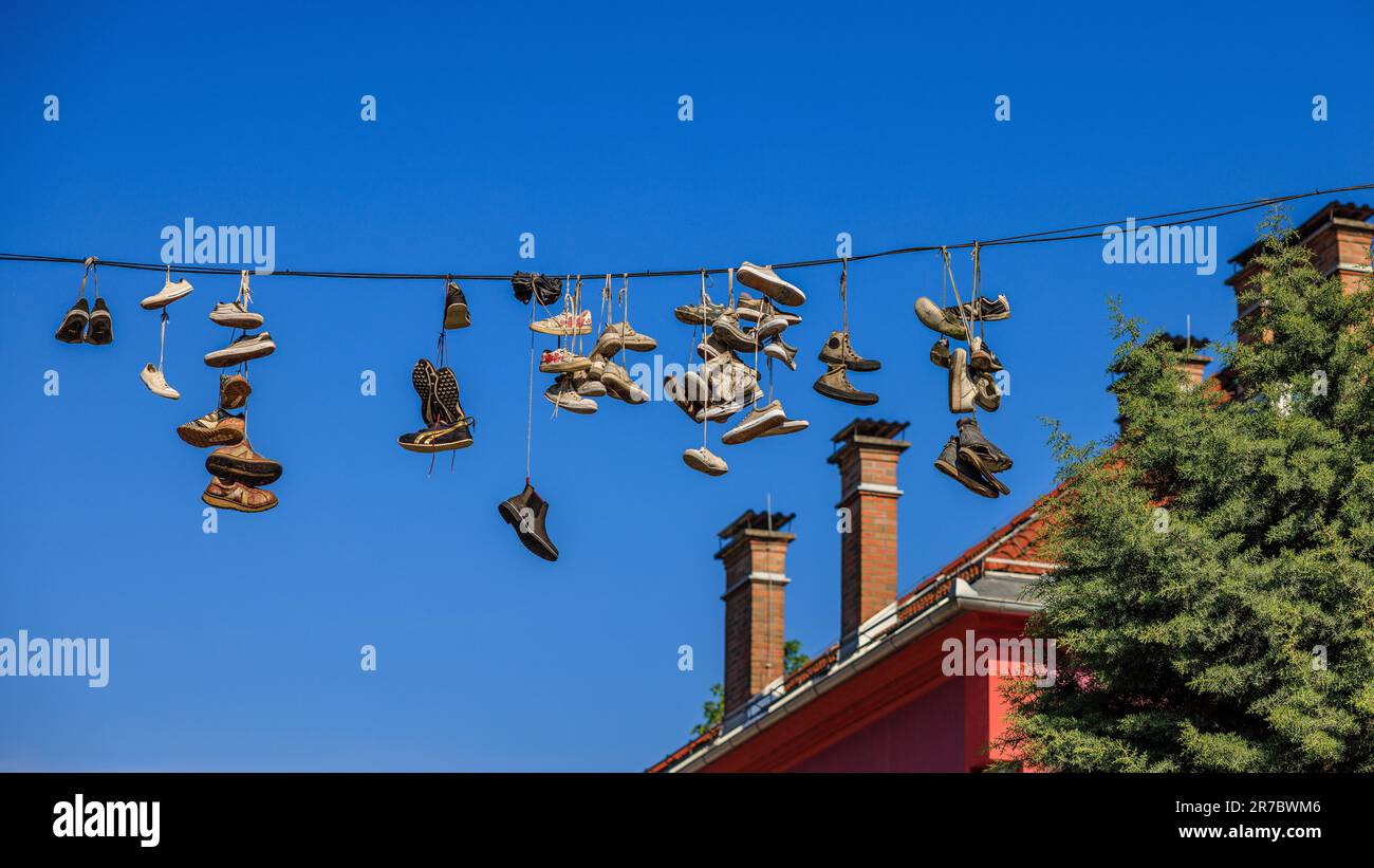street art installation of many pairs of shoes and trainers hanging by their laces from a telegraph wire in the rooftops of metelkova ljubljiana Stock Photo