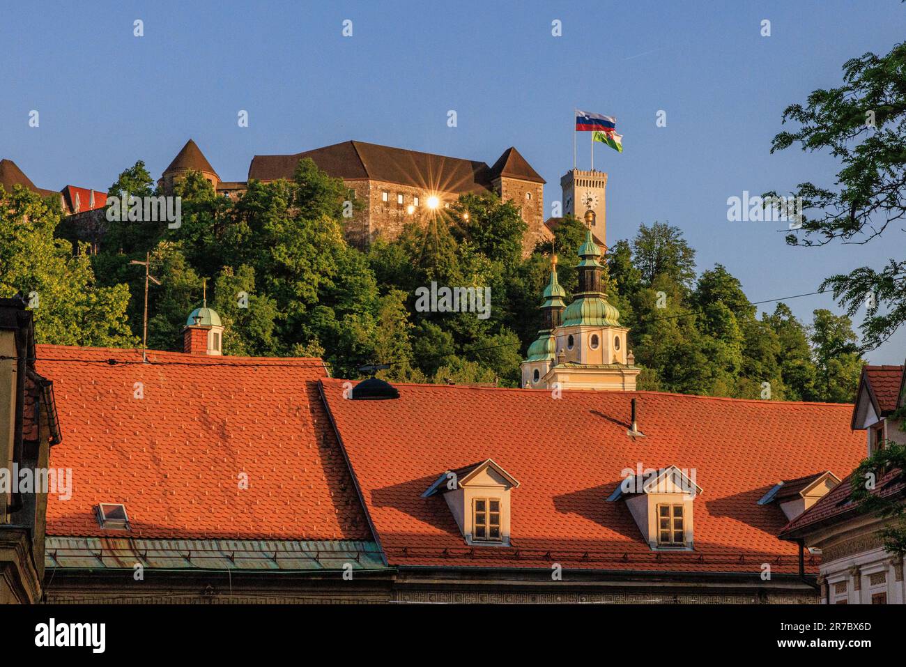 early evening setting sun is reflected as a sunburst in a window of ljubljiana castle on top of castle hill Stock Photo