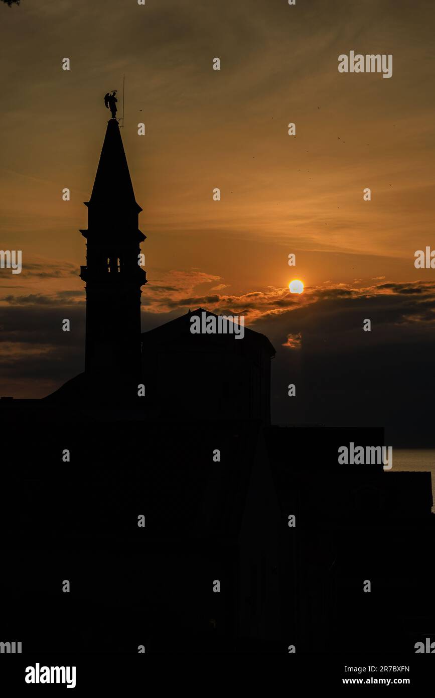 the bell tower of st george's church in piran in silhouette against a ...