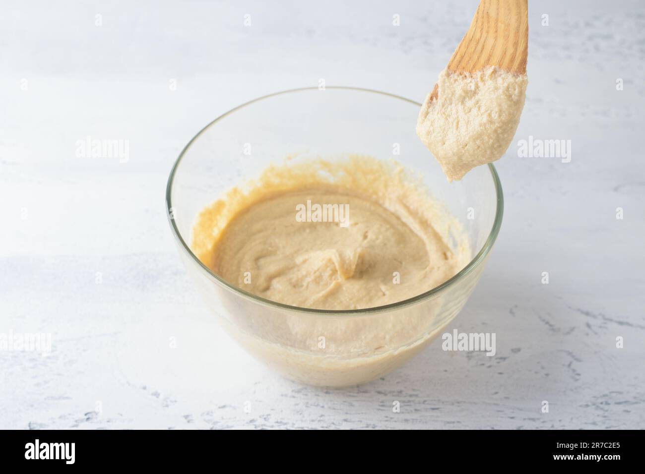 Glass bowl with dough and spatula, dough texture and consistency, light blue background. The stage of preparing homemade choux pastry Stock Photo