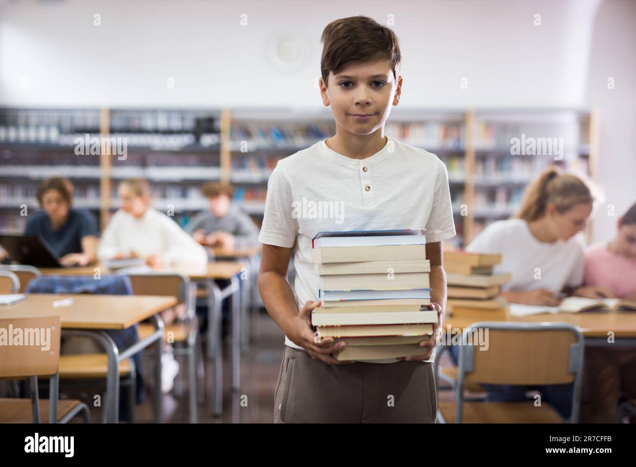 Teenager boy standing with a stack of books in library Stock Photo - Alamy