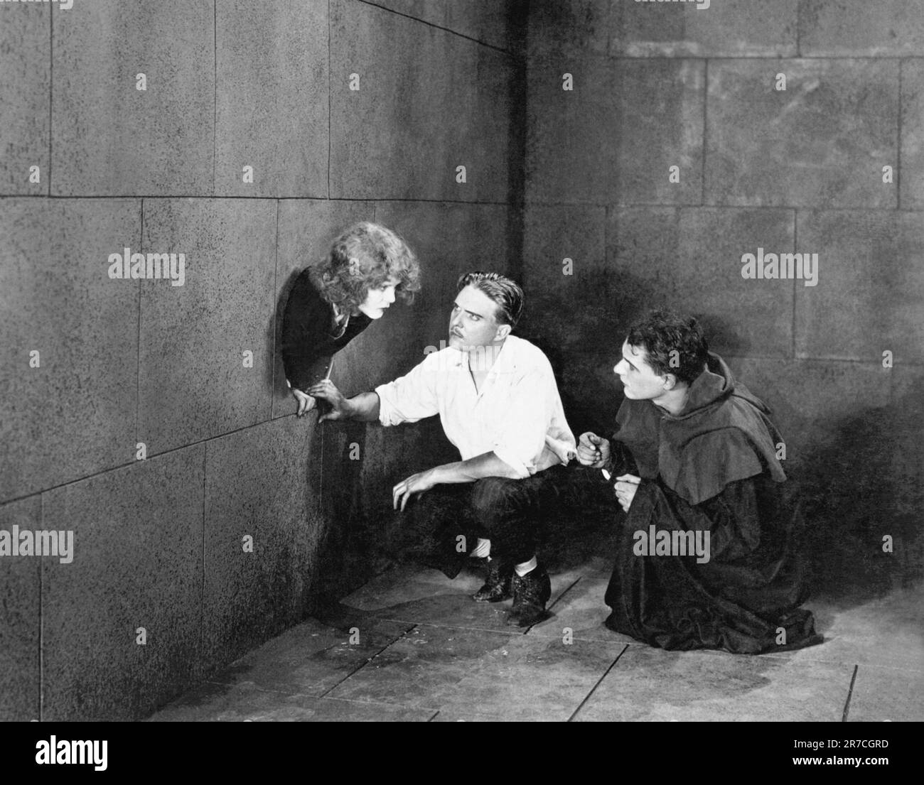 Hollywood, California:  c. 1918 A scene in an early silent movie still where two men in a room converse with a woman sticking her head out of a hole in the wall. Stock Photo