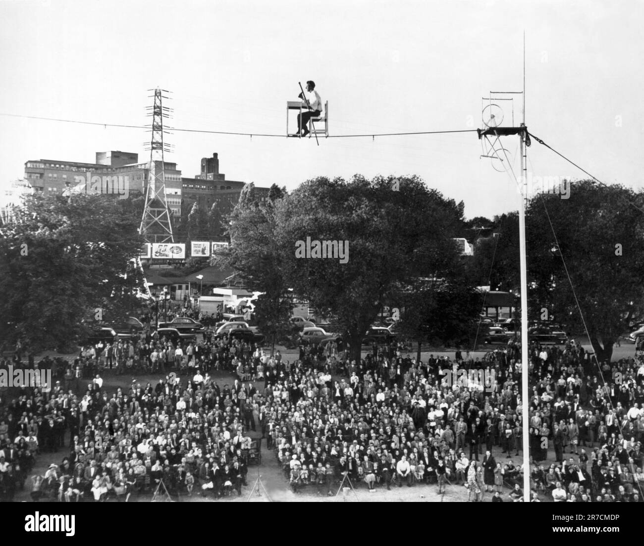 United States:  c. 1947 A man sits on a chair at a desk on a tightrope. Stock Photo