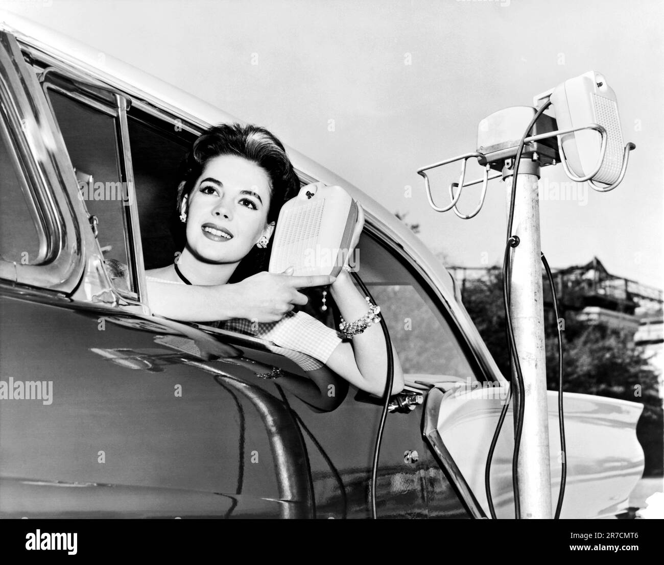 Hollywood, California: 1957. Natalie Wood displays the new drive in-movie speakers as she leans out of her car window. Stock Photo