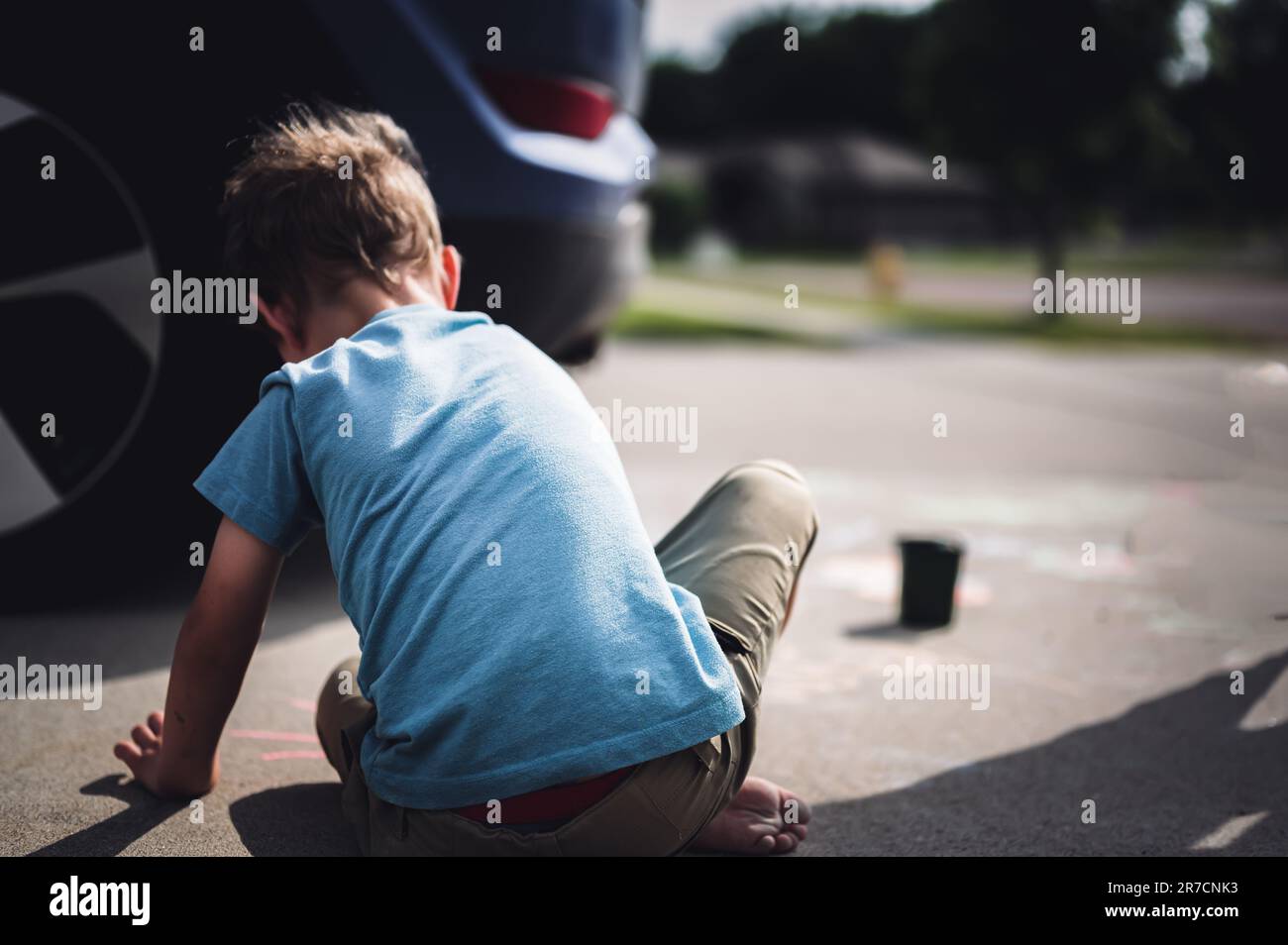 Children sitting on a driveway behind a vehicle in a blind spot out of view of the driver.  Stock Photo