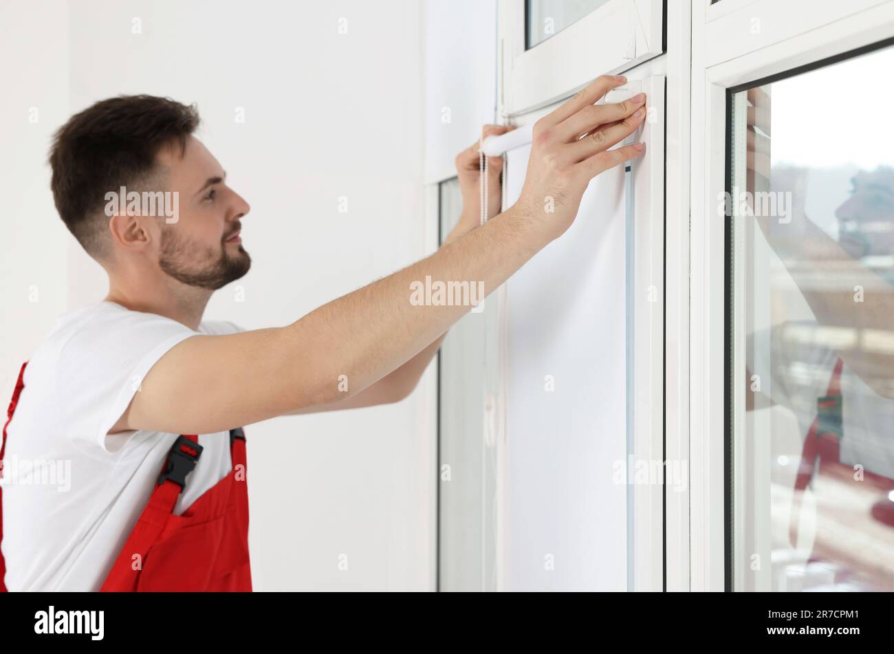 Worker in uniform installing roller window blind indoors, focus on hands Stock Photo