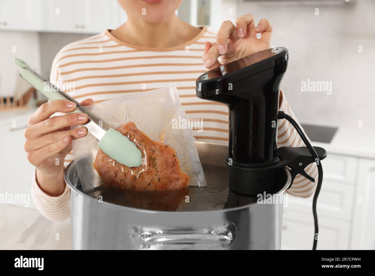 Woman putting vacuum packed meat into pot and using thermal immersion