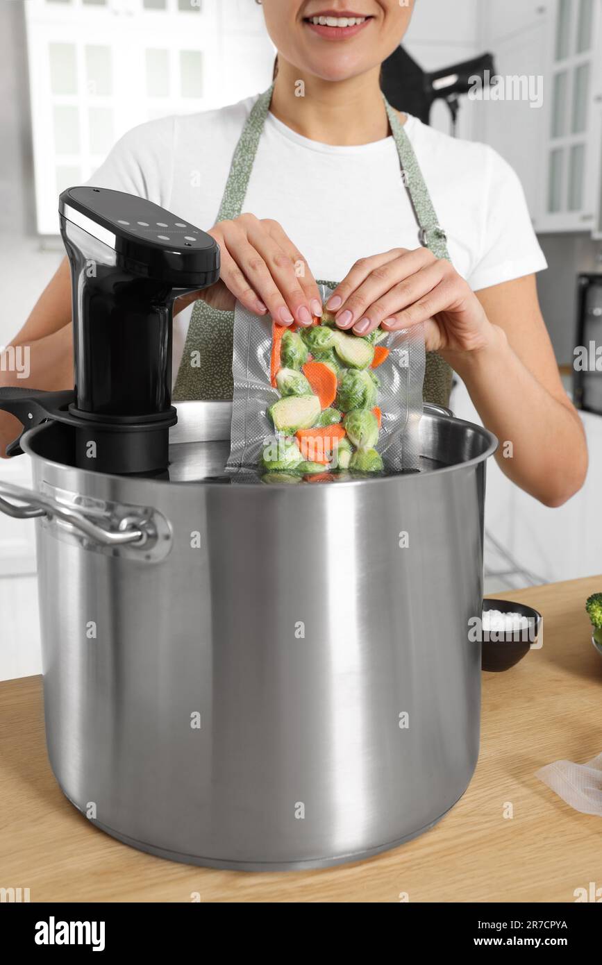 Woman putting vacuum packed vegetables into pot with sous vide cooker
