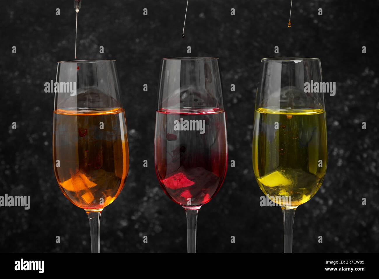 Different food coloring pouring into glasses on grey background Stock Photo