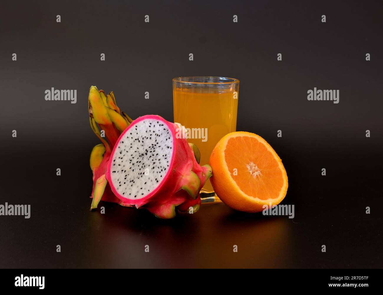 A tall glass of fruit juice and half a ripe orange and pitaya on a black background. Close-up. Stock Photo