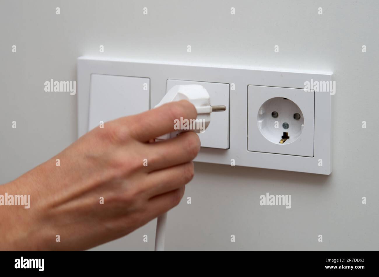 Woman's hand plugs an electric plug into a socket Stock Photo