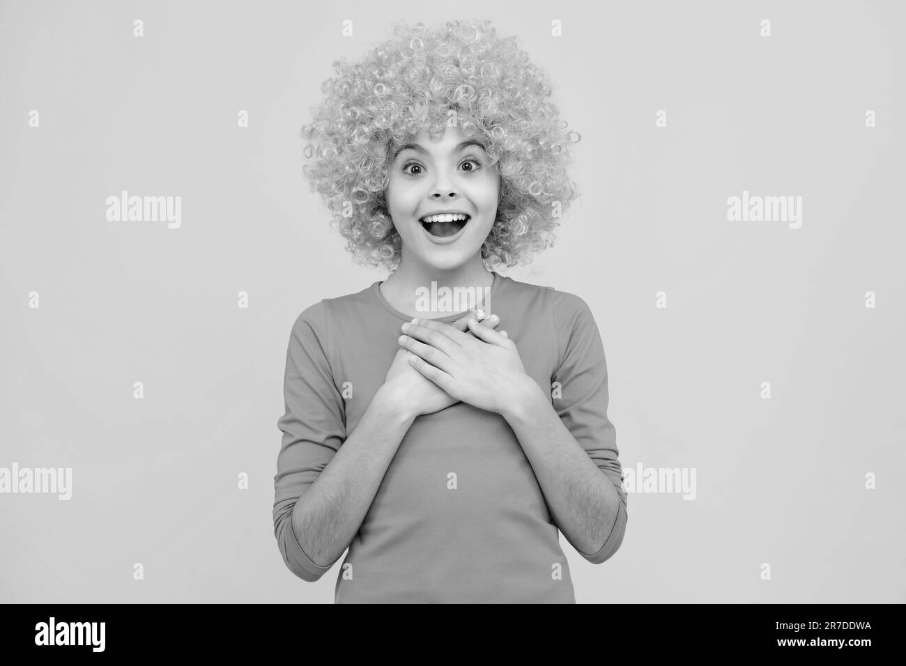 Teenage girl with yellow wig. Funny child wearing orange curly wig hair. Excited teenager, glad amazed and overjoyed emotions. Stock Photo