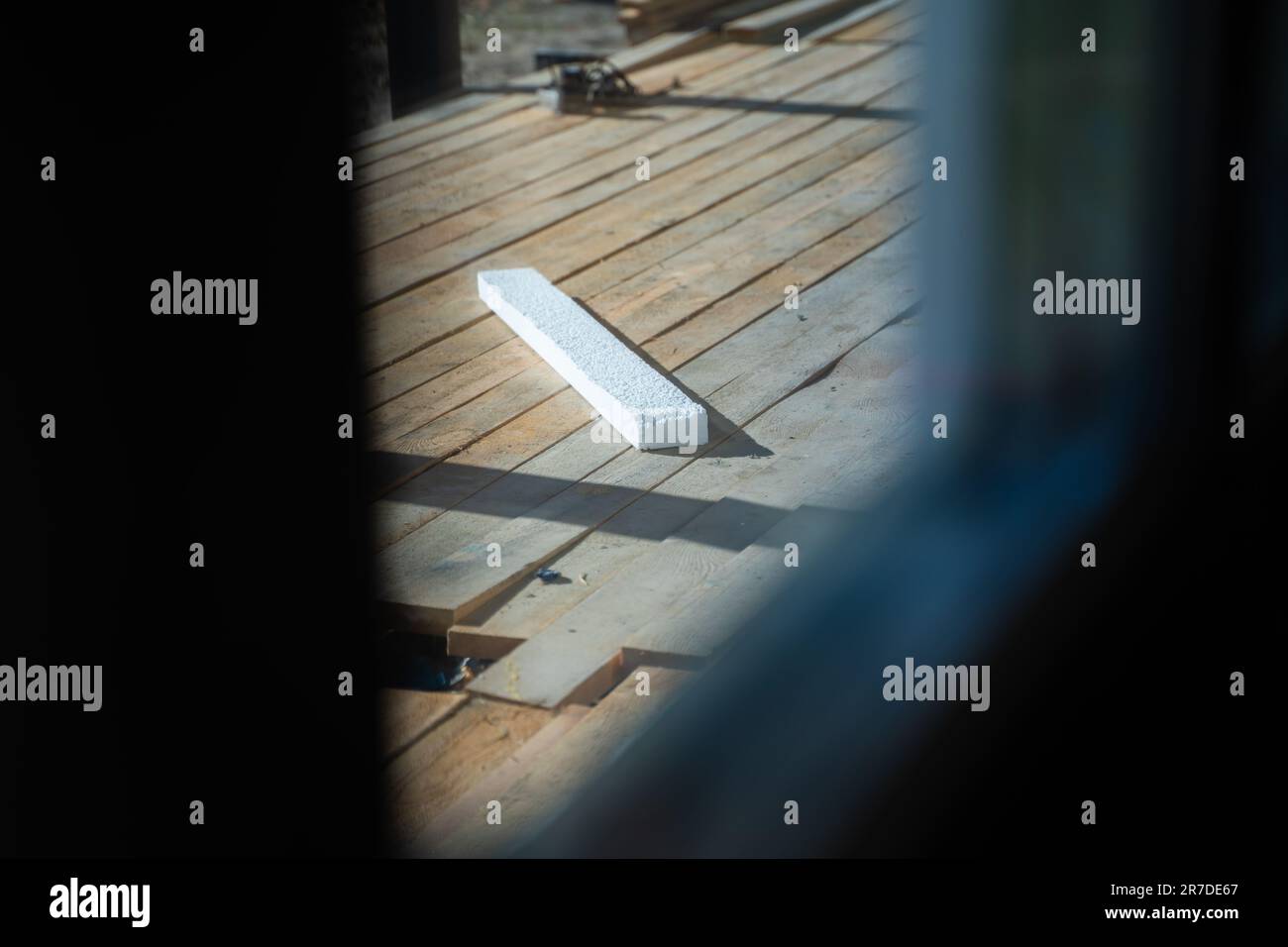A thin piece of white polystyrene foam after the insulation of the house lies on wooden boards on the terrace of a private house, view from the window Stock Photo